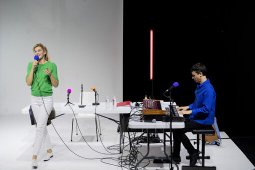 Un homme,assis, joue du piano à droite de l'image, et une femme chante, debout, à gauche.