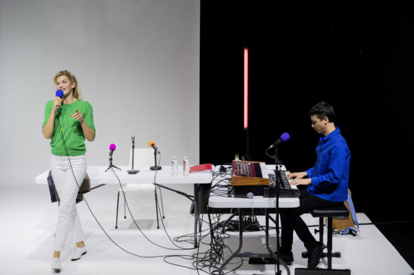 Un homme,assis, joue du piano à droite de l'image, et une femme chante, debout, à gauche.