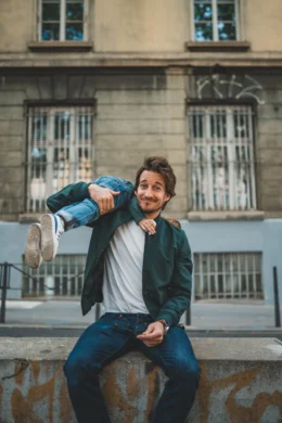 Un homme est assis et regarde la caméra, avec un enfant sur son épaule, en souriant.