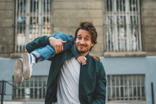 Un homme est assis et regarde la caméra, avec un enfant sur son épaule, en souriant.