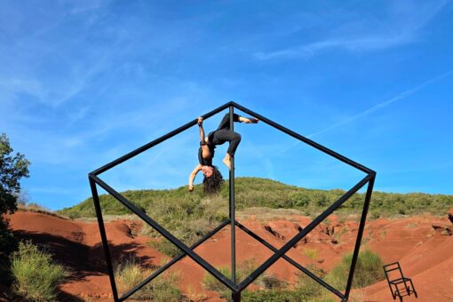 Une structure en métal, sorte de cube géant, est au centre de l'image. Une femme y est suspendue, par les jambes, comme en cochon pendu.