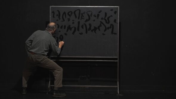 Un homme dessine des motifs abstraits sombres sur un tableau noir