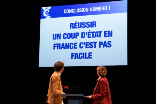 Un homme et une femme, tournés devant un écran, où on peut lire "Réussir un coup d'état en France n'est pas facile